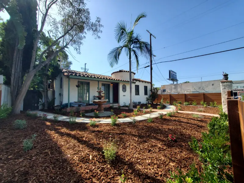 Fresh mulch and new plantings across the front yard of a white house with palm trees