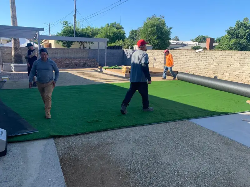 Crew rolling out and fitting artificial turf on a prepared base